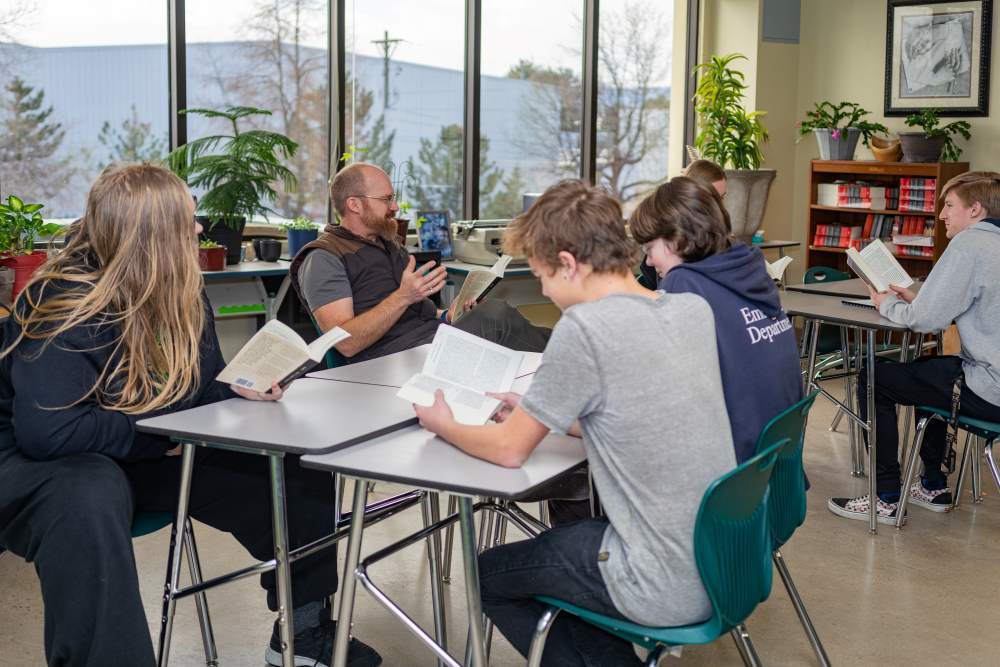 Four high school students at Twin Peaks Classical Charter Academy tuition-free public school sitting at classroom tables discussing books with a teacher